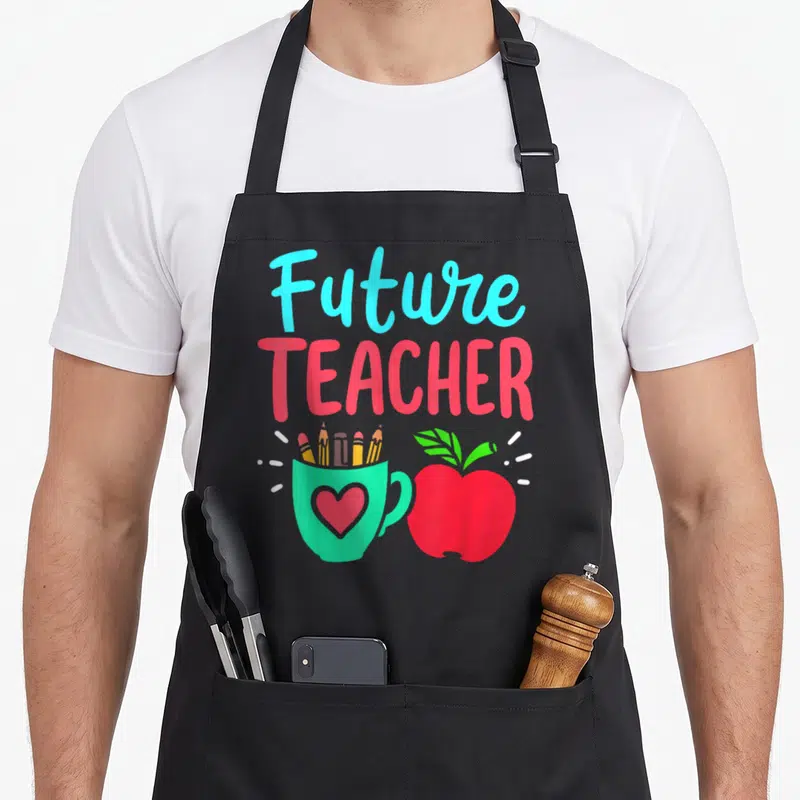 Education teacher apron - Future TEACHER text above green pencil cup and red apple cartoon — shown on a black cotton canvas apron against a white background