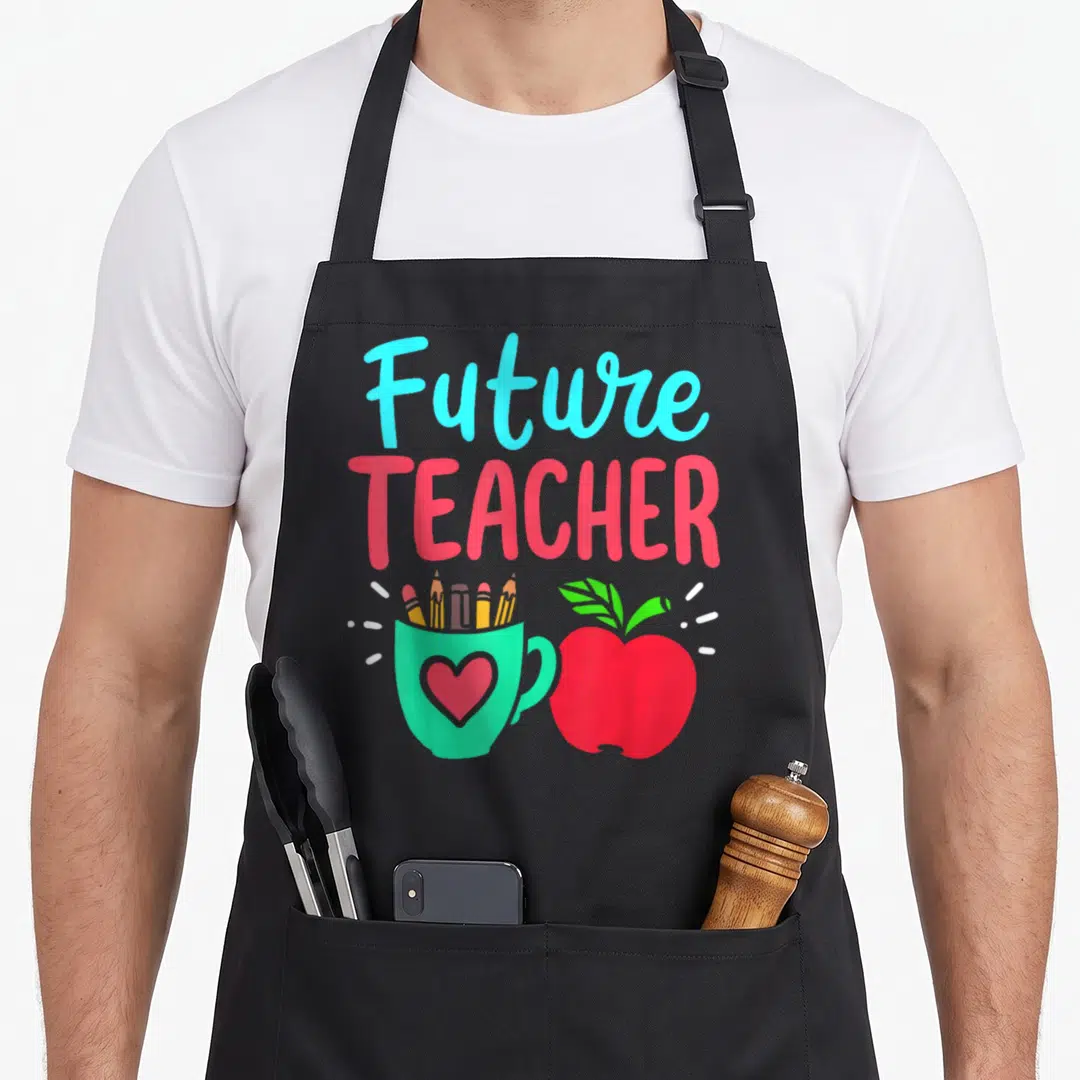 Education teacher apron - Future TEACHER text above green pencil cup and red apple cartoon — shown on a black cotton canvas apron against a white background