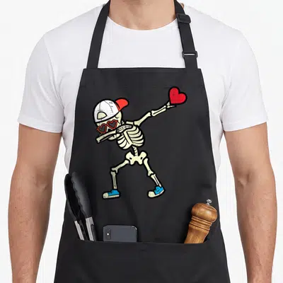 Skeleton valentine's day apron - Dabbing skeleton with heart sunglasses holding red heart, distressed print — shown on a black cotton canvas apron against a white background