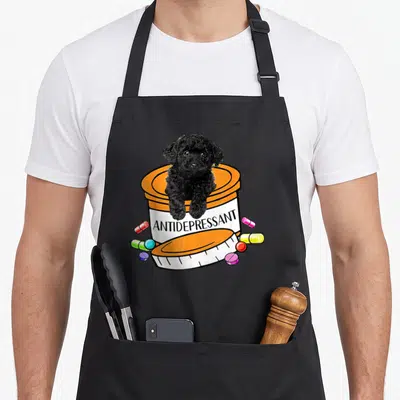 Antidepressant basset hound apron - Black dog sitting in orange pill bottle labeled antidepressant with scattered pills — shown on a black cotton canvas apron against a white background