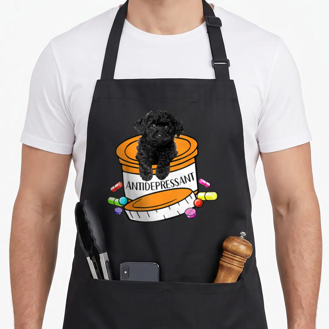 Antidepressant basset hound apron - Black dog sitting in orange pill bottle labeled antidepressant with scattered pills — shown on a black cotton canvas apron against a white background