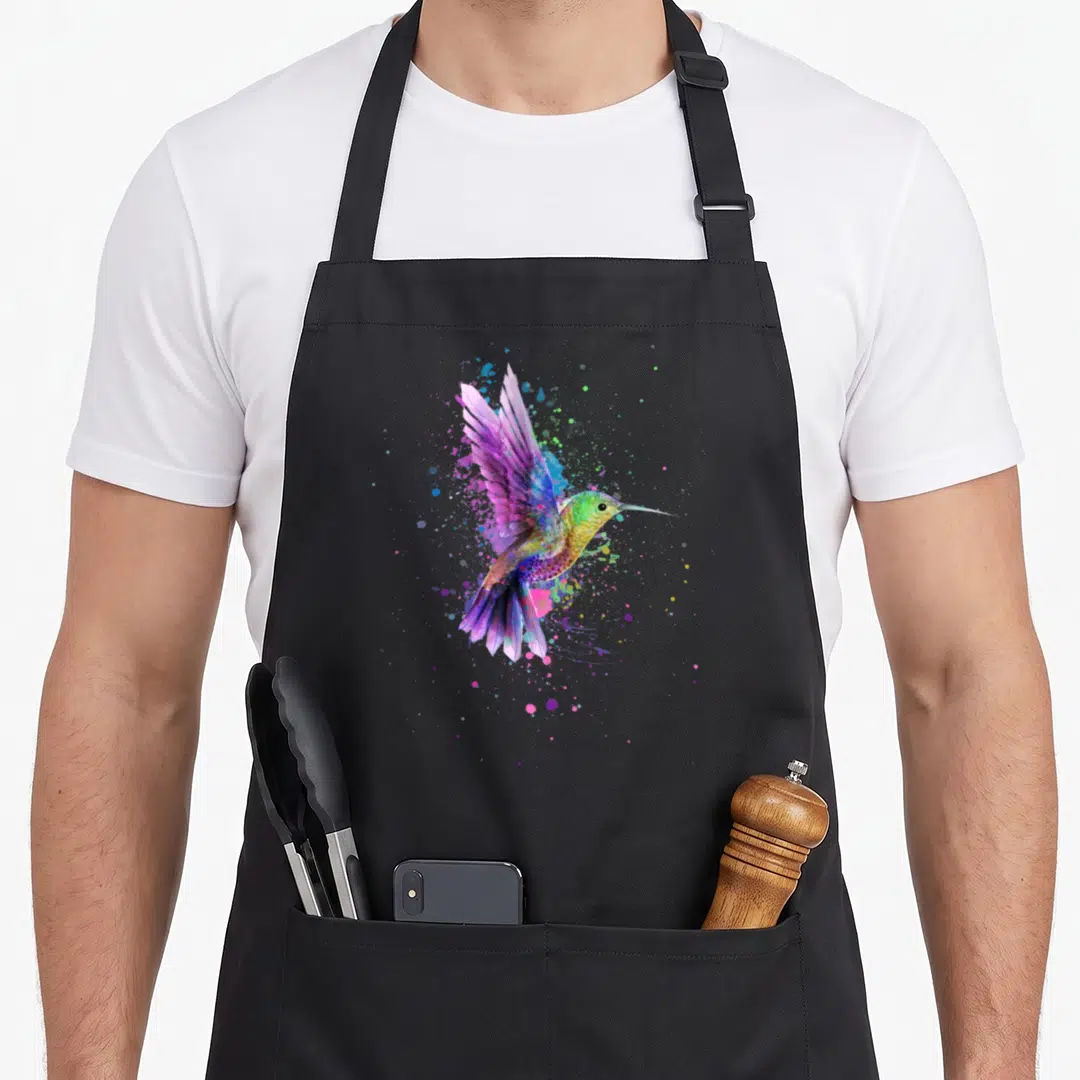 Watercolor hummingbird lover apron - Rainbow watercolor hummingbird with purple blue green yellow pink paint splatters — shown on a black cotton canvas apron against a white background