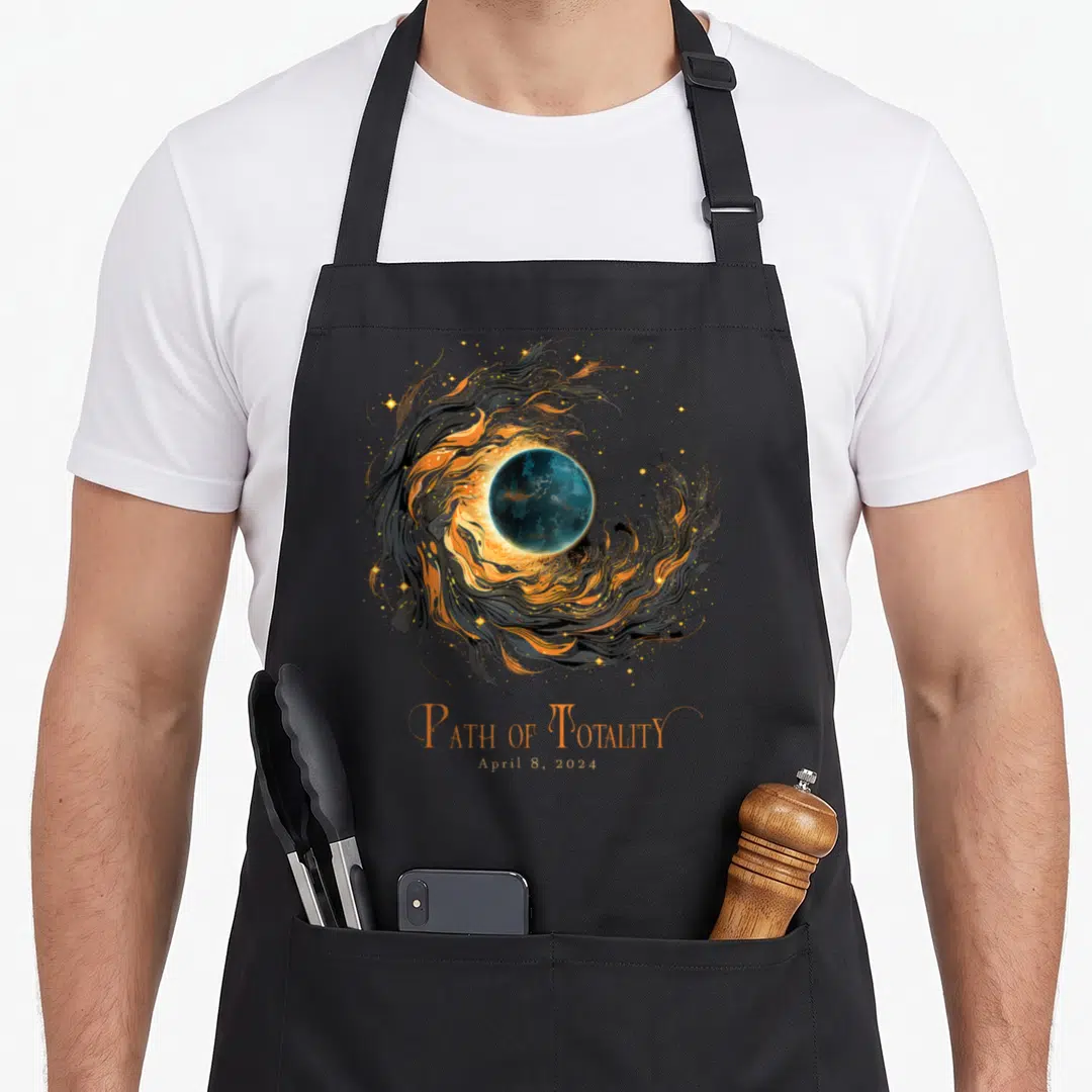 Solar eclipse april apron - Blue planet surrounded by orange and black swirls with text Path of Totality April 8 2024 — shown on a black cotton canvas apron against a white background