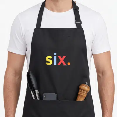 6th six birthday apron - Colorful text six in yellow blue red and orange with two front pockets — shown on a black cotton canvas apron against a white background