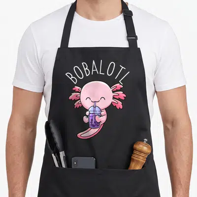 Bobalotl milk aprons - Pink cartoon axolotl drinking purple boba tea with white arched text BOBALOTL — shown on a black cotton canvas apron against a white background