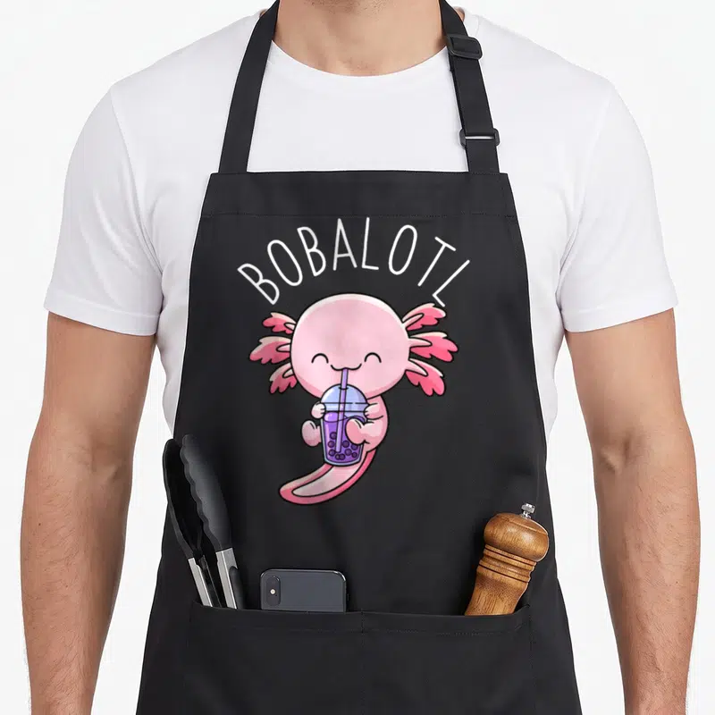 Bobalotl milk aprons - Pink cartoon axolotl drinking purple boba tea with white arched text BOBALOTL — shown on a black cotton canvas apron against a white background