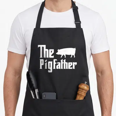 Pigfather farming apron - White pig silhouette next to The PigFather text in minimalist font — shown on a black cotton canvas apron against a white background