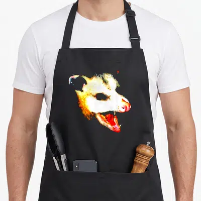 Possum face apron - Watercolor animal head facing right with open mouth in white yellow orange red and blue — shown on a black cotton canvas apron against a white background