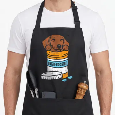 Antidepressant sausage apron - Brown dachshund in orange pill bottle with blue pills and antidepressant text — shown on a black cotton canvas apron against a white background