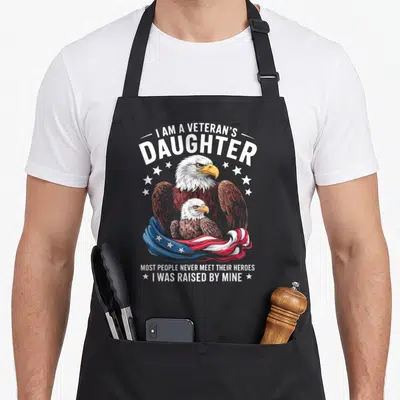 Veteran daughter people meet apron - Bald eagle and chick with patriotic flag and text about being raised by a veteran — shown on a black cotton canvas apron against a white background