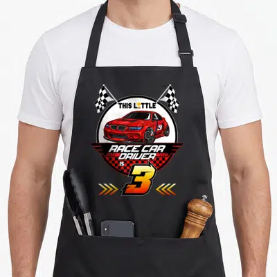 Birthday 3rd car apron - Red race car in white circle with checkered flags and number 3 text — shown on a black cotton canvas apron against a white background