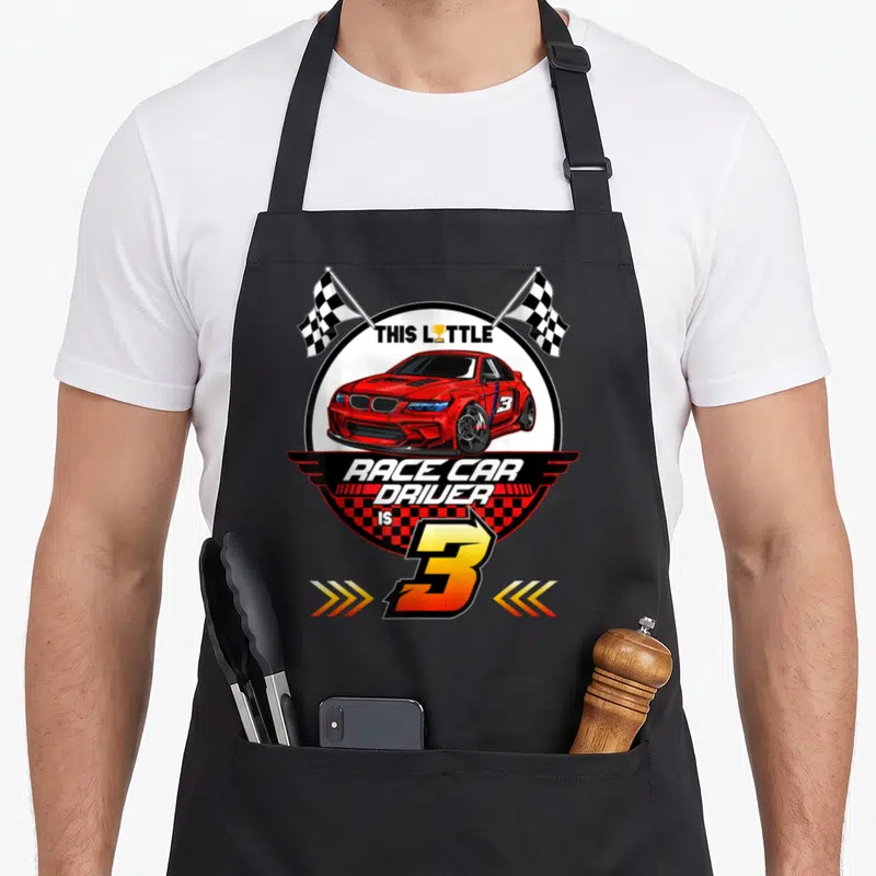 Birthday 3rd car apron - Red race car in white circle with checkered flags and number 3 text — shown on a black cotton canvas apron against a white background
