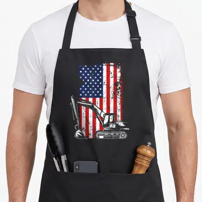 July american flag apron - Distressed American flag with white excavator silhouette overlay on red, white, and blue — shown on a black cotton canvas apron against a white background