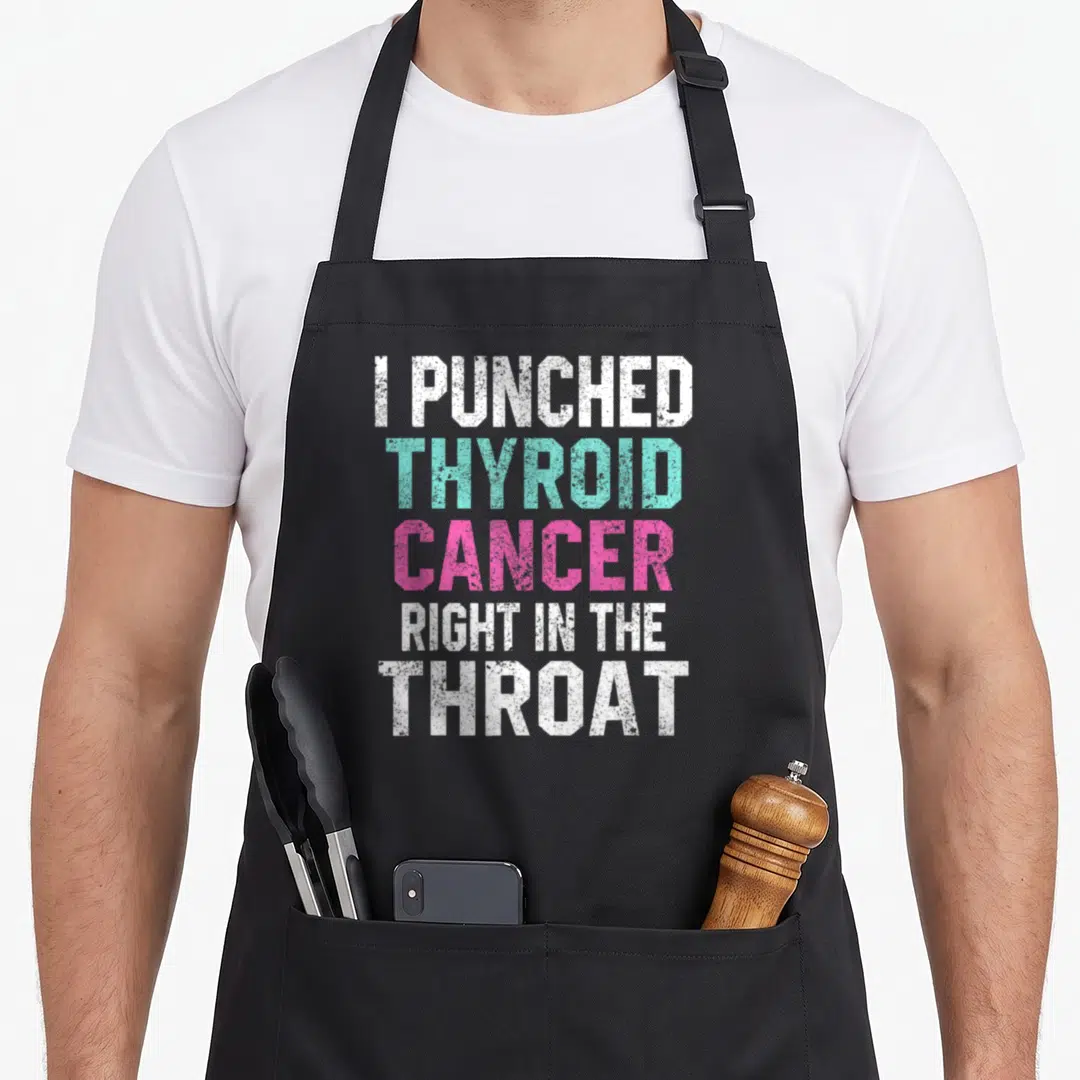 Punched thyroid apron - Stacked text I Punched Thyroid Cancer Right In The Throat in white teal and pink block letters — shown on a black cotton canvas apron against a white background