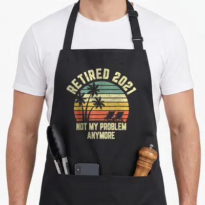 Cool problem retirement apron - Retro striped sunset with palm tree silhouettes and retired 2021 text — shown on a black cotton canvas apron against a white background