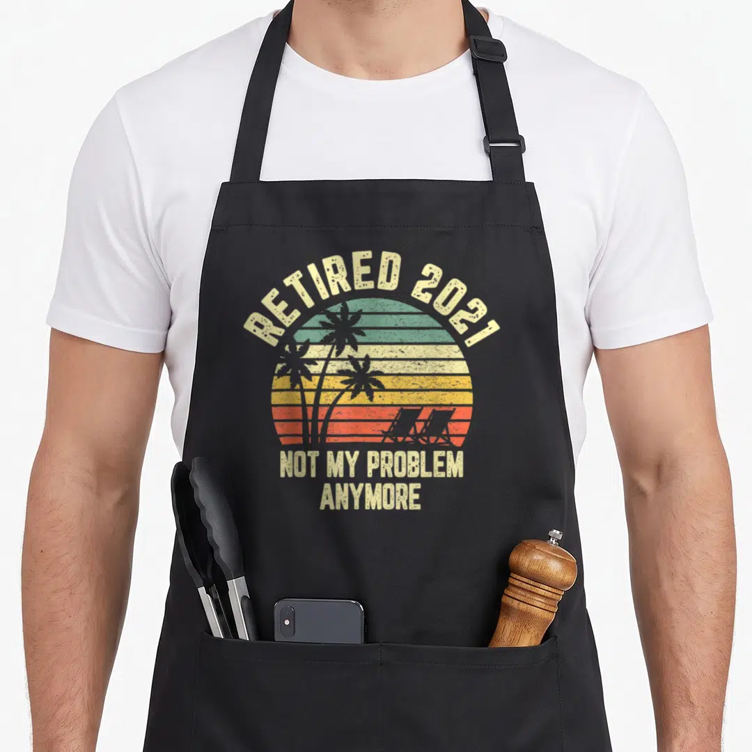 Cool problem retirement apron - Retro striped sunset with palm tree silhouettes and retired 2021 text — shown on a black cotton canvas apron against a white background