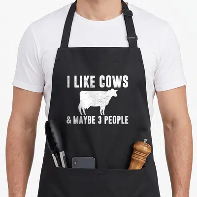 Maybe cow apron - White distressed cow silhouette between text I LIKE COWS and maybe 3 people — shown on a black cotton canvas apron against a white background