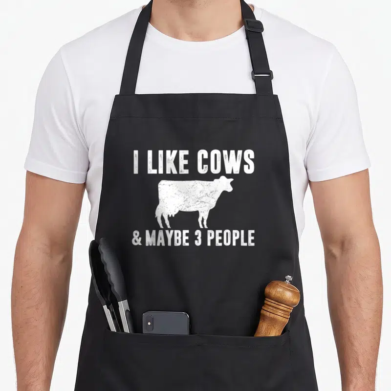 Maybe cow apron - White distressed cow silhouette between text I LIKE COWS and maybe 3 people — shown on a black cotton canvas apron against a white background
