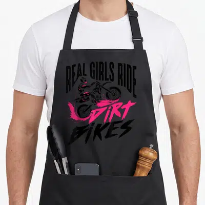 Racer bike apron - Real Girls Ride Dirt Bikes text with rider and pink splash — shown on a black cotton canvas apron against a white background
