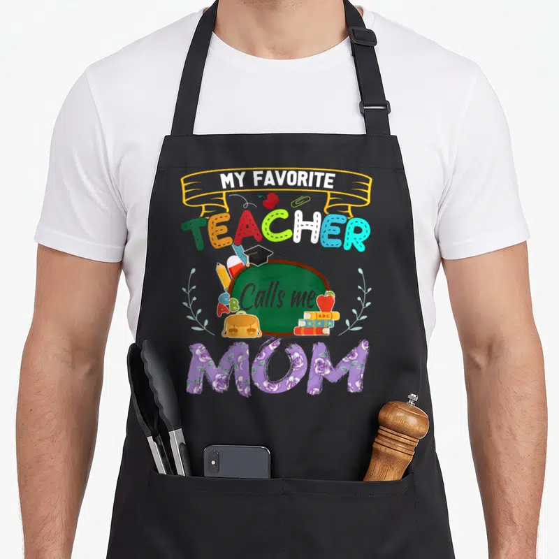 Call cute teacher apron - My Favorite Teacher Calls Me Mom graphic with chalkboard, colorful letters, and floral Mom — shown on a black cotton canvas apron against a white background