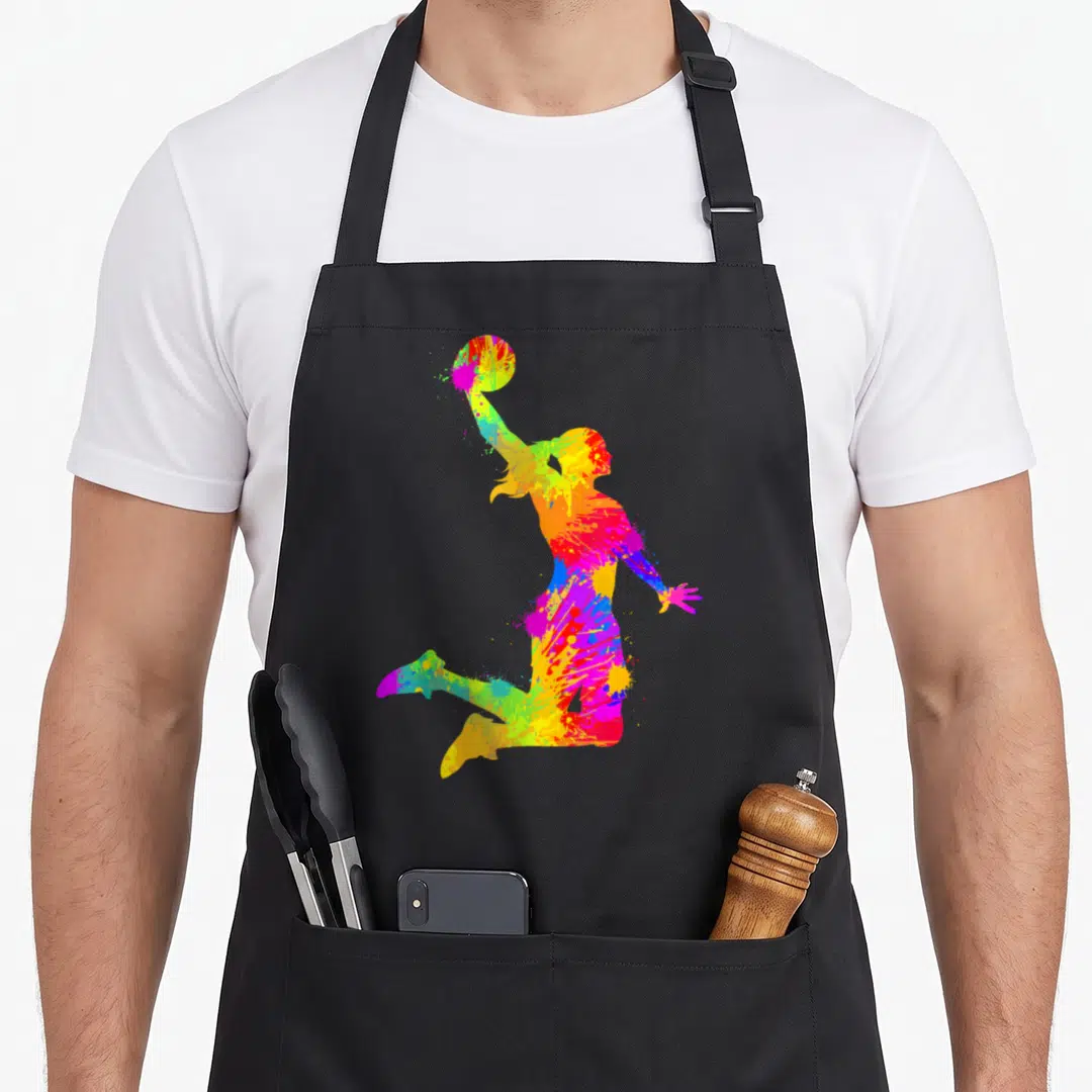 Cute player basketball apron - Jumping basketball player silhouette filled with multicolored paint splatters in red — shown on a black cotton canvas apron against a white background