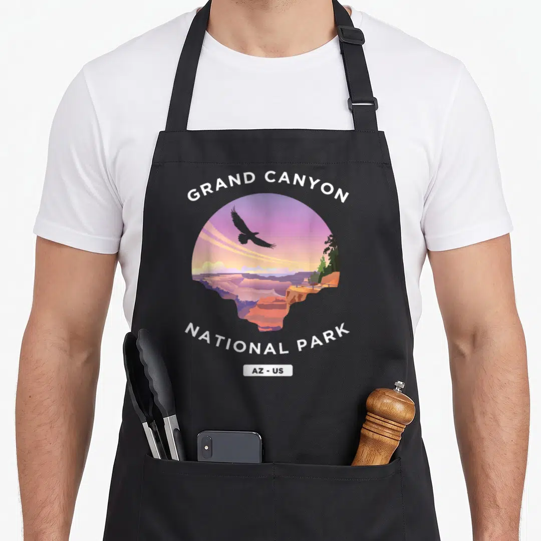 Grand us aprons - Retro Grand Canyon circular landscape with purple sky, eagle silhouette, and white arched text — shown on a black cotton canvas apron against a white background