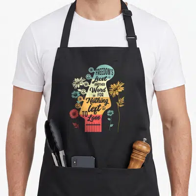 Freedom another word for apron - Striped guitar headstock with stacked text FREEDOM'S just ANOTHER Word FOR Nothing — shown on a black cotton canvas apron against a white background