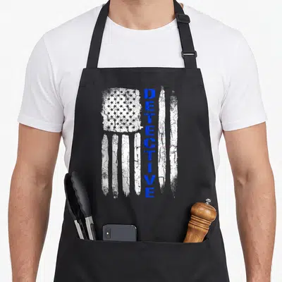 Detective american flag apron - Vertical blue DETECTIVE text beside distressed white flag with vertical stripes — shown on a black cotton canvas apron against a white background