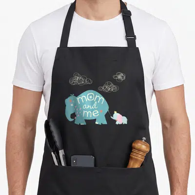 Mother elephant print apron - Blue mom elephant with mom and me text, pink hearts, baby elephant, three scribbled clouds — shown on a black cotton canvas apron against a white background