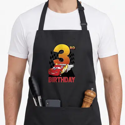Youth 3rd car apron - Red race car with flames, large number 3, checkered flag, and BIRTHDAY text — shown on a black cotton canvas apron against a white background