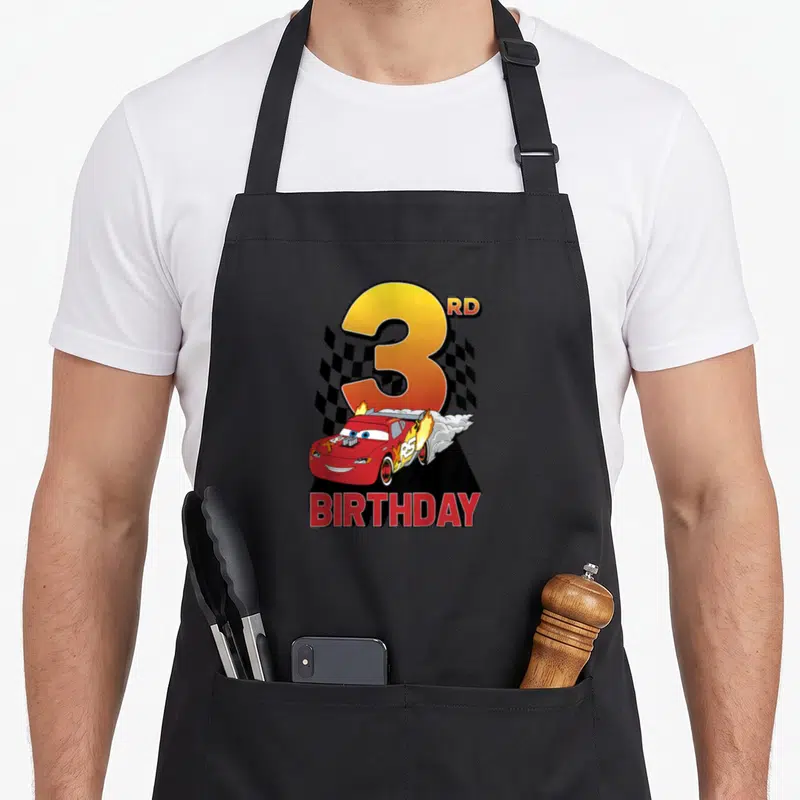 Youth 3rd car apron - Red race car with flames, large number 3, checkered flag, and BIRTHDAY text — shown on a black cotton canvas apron against a white background