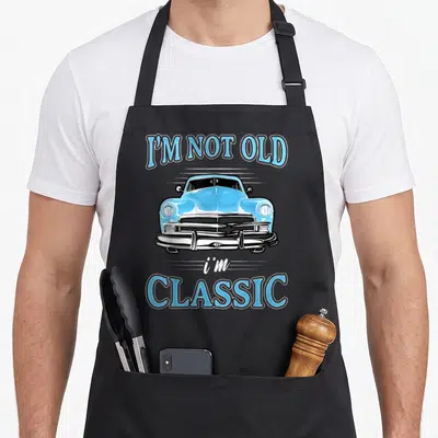 Cars apron for dad - Light blue cartoon classic car flanked by arched text I'M NOT OLD and i'm CLASSIC — shown on a black cotton canvas apron against a white background