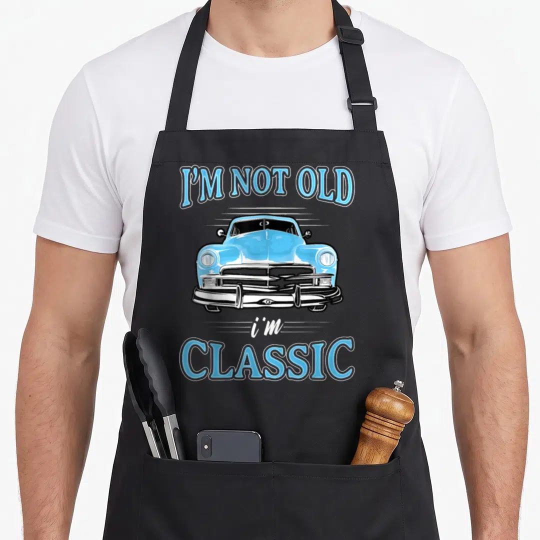 Cars apron for dad - Light blue cartoon classic car flanked by arched text I'M NOT OLD and i'm CLASSIC — shown on a black cotton canvas apron against a white background