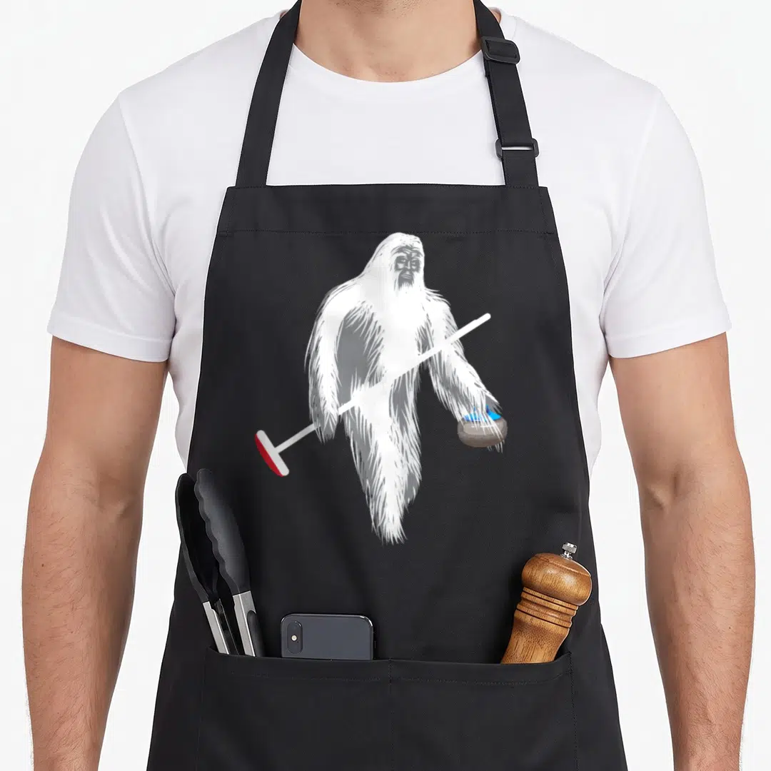 Curling bigfoot apron - White Yeti holding curling broom with red head and blue handled stone — shown on a black cotton canvas apron against a white background