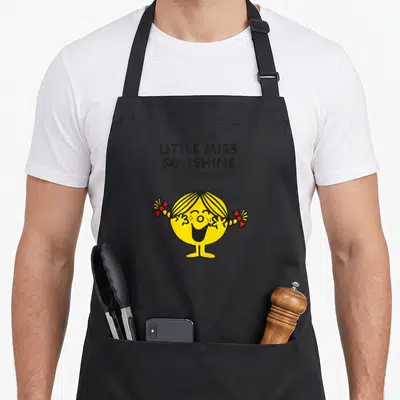 Miss mr apron - LITTLE MISS SUNSHINE text above yellow cartoon girl with red bows — shown on a black cotton canvas apron against a white background