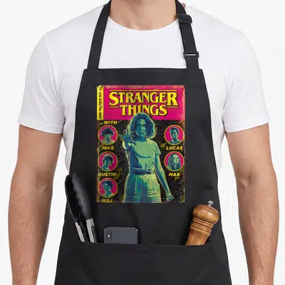Shot stranger apron - Retro Stranger Things comic cover with girl and four named character portraits in magenta — shown on a black cotton canvas apron against a white background