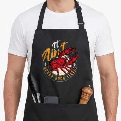 Suck cajun aprons - Red lobster illustration inside blue-grey circle with anchors and orange script text It Ain't Gonna — shown on a black cotton canvas apron against a white background