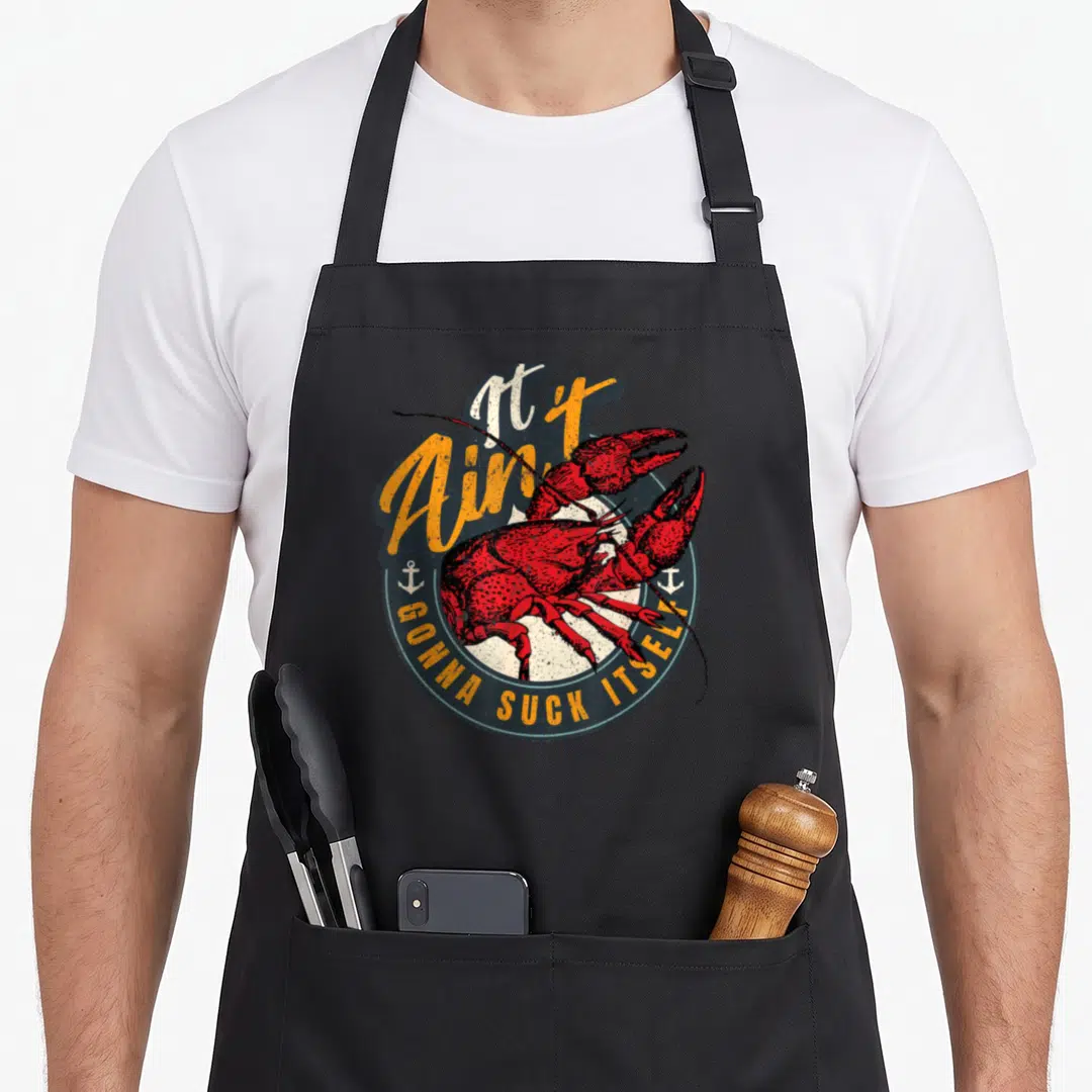 Suck cajun aprons - Red lobster illustration inside blue-grey circle with anchors and orange script text It Ain't Gonna — shown on a black cotton canvas apron against a white background