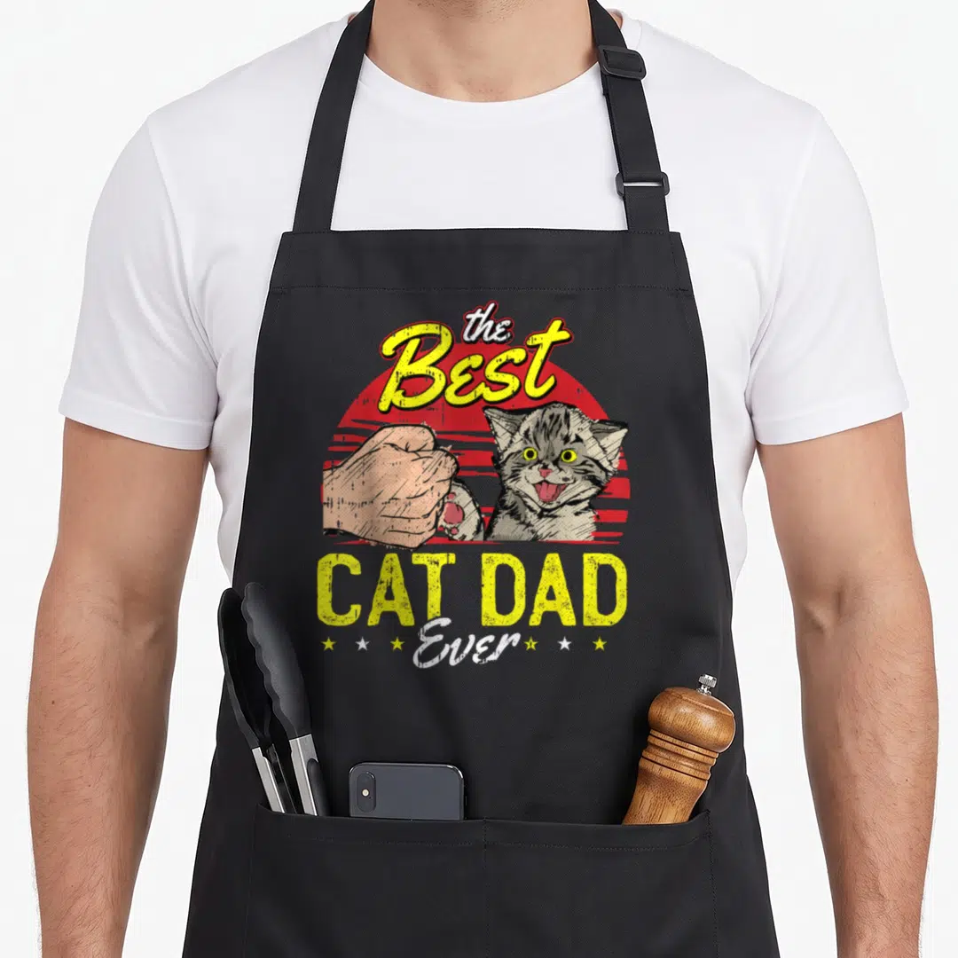 Kitty father day apron - Grey kitten fist bumping human hand under Best Cat Dad Ever text over red striped sun — shown on a black cotton canvas apron against a white background