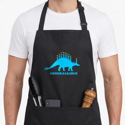 Hanukkah dinosaur apron - Blue stegosaurus with yellow candles and menorasaurus text below — shown on a black cotton canvas apron against a white background