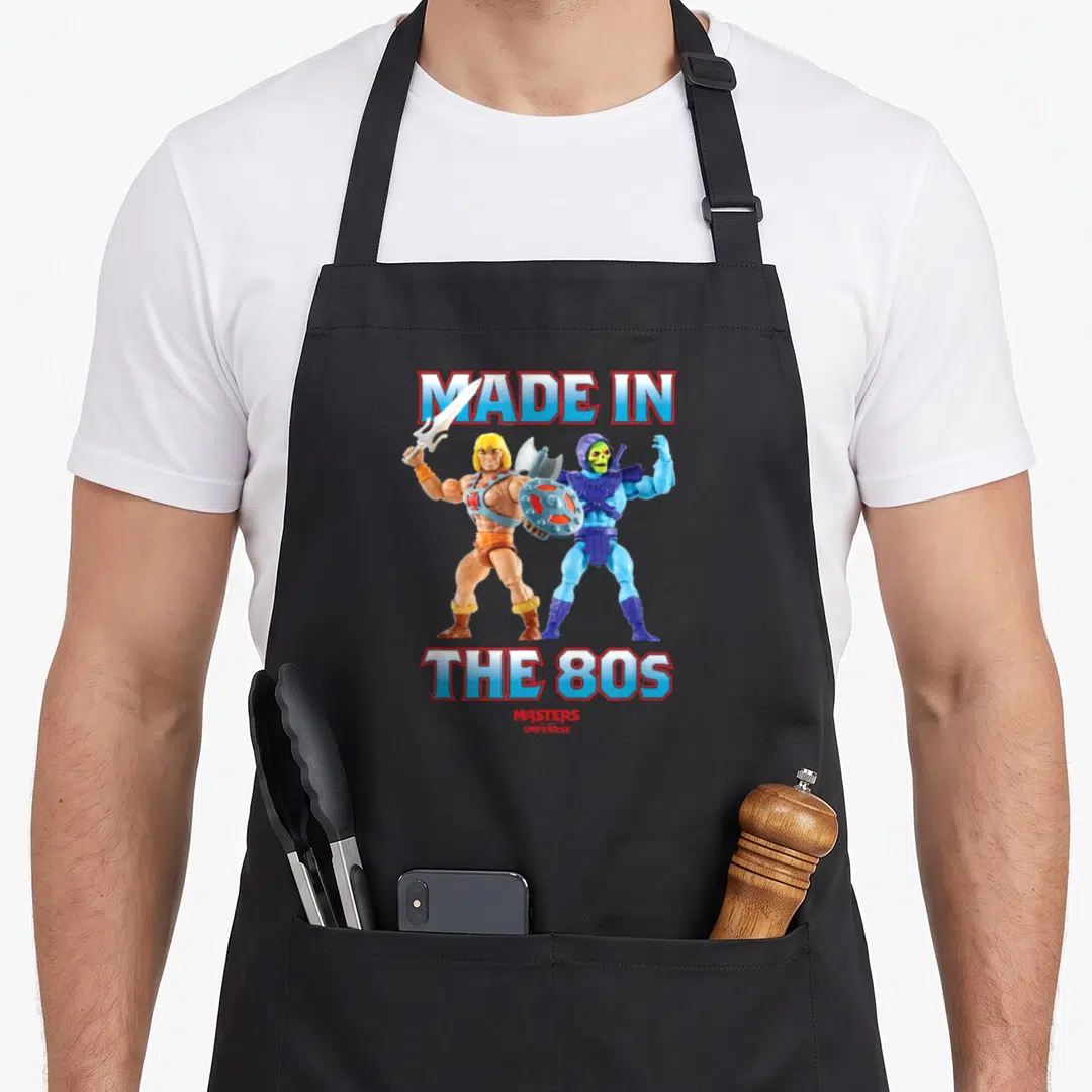 Funny 80s apron - He-Man and Skeletor standing back-to-back under Made in The 80s text — shown on a black cotton canvas apron against a white background