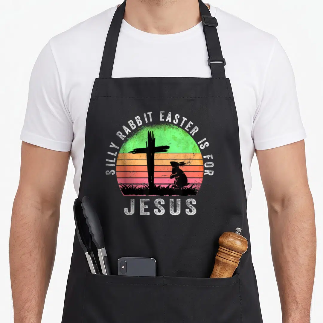 Christian rabbit apron - Silly Rabbit Easter is for Jesus text over distressed sunset circle with black cross — shown on a black cotton canvas apron against a white background
