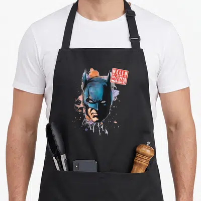 Come animal apron - Blue Batman cowl with red HELLO MY NAME IS BATMAN name tag graphic — shown on a black cotton canvas apron against a white background