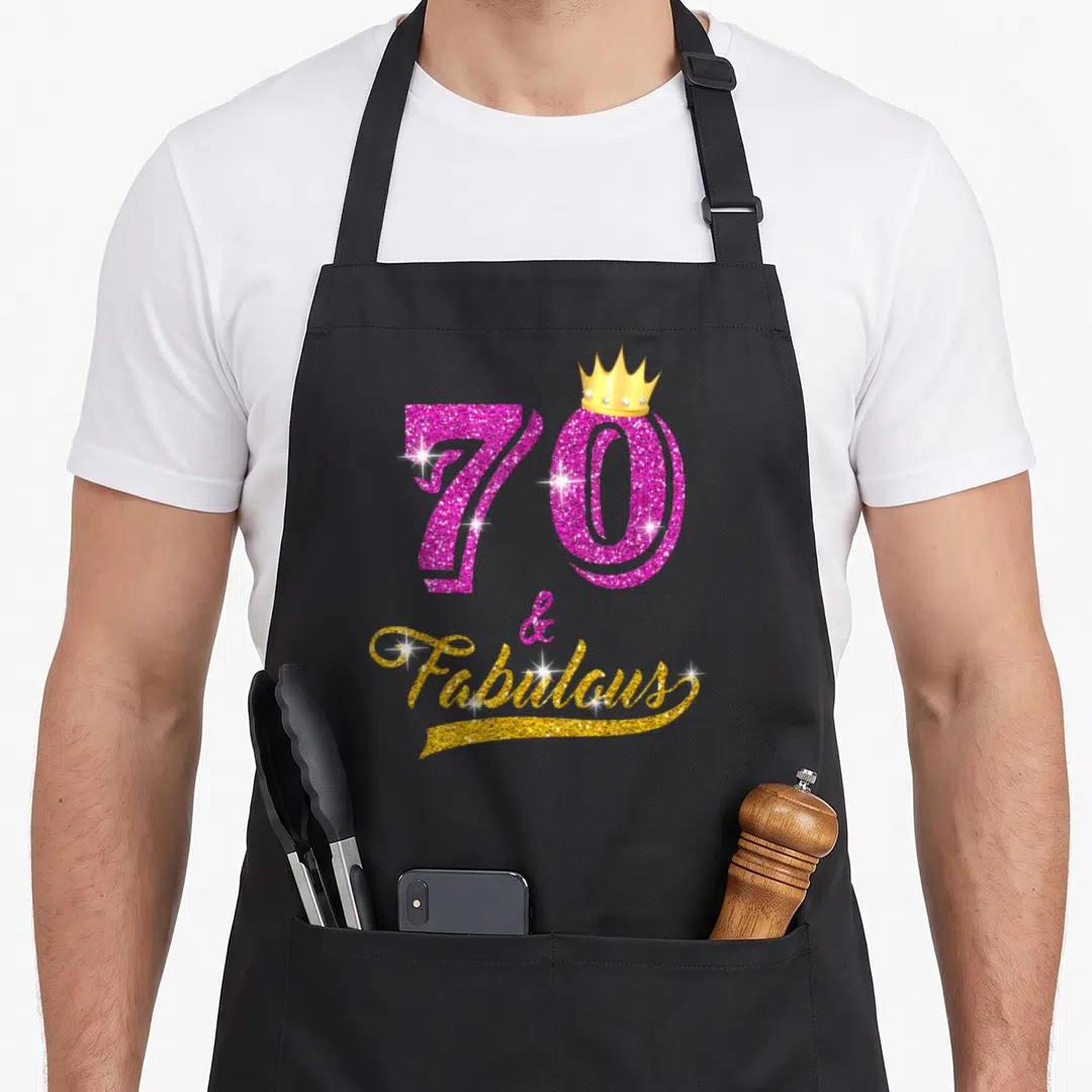 Fabulous 70th birthday apron - Pink glitter 70 with gold crown and Fabulous script — shown on a black cotton canvas apron against a white background