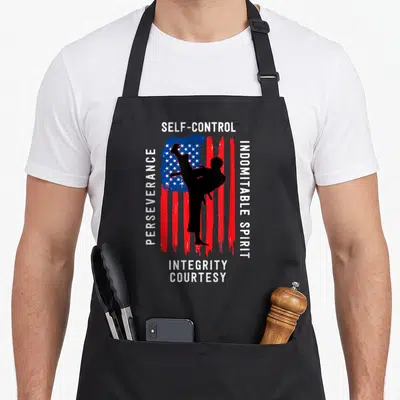 Taekwondo kung apron - Martial artist kicking silhouette over distressed flag with five tenet words in white text — shown on a black cotton canvas apron against a white background