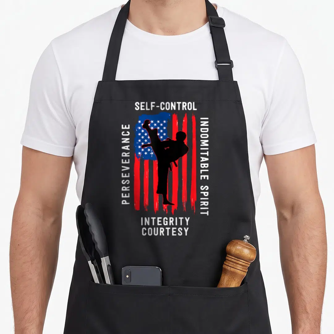 Taekwondo kung apron - Martial artist kicking silhouette over distressed flag with five tenet words in white text — shown on a black cotton canvas apron against a white background