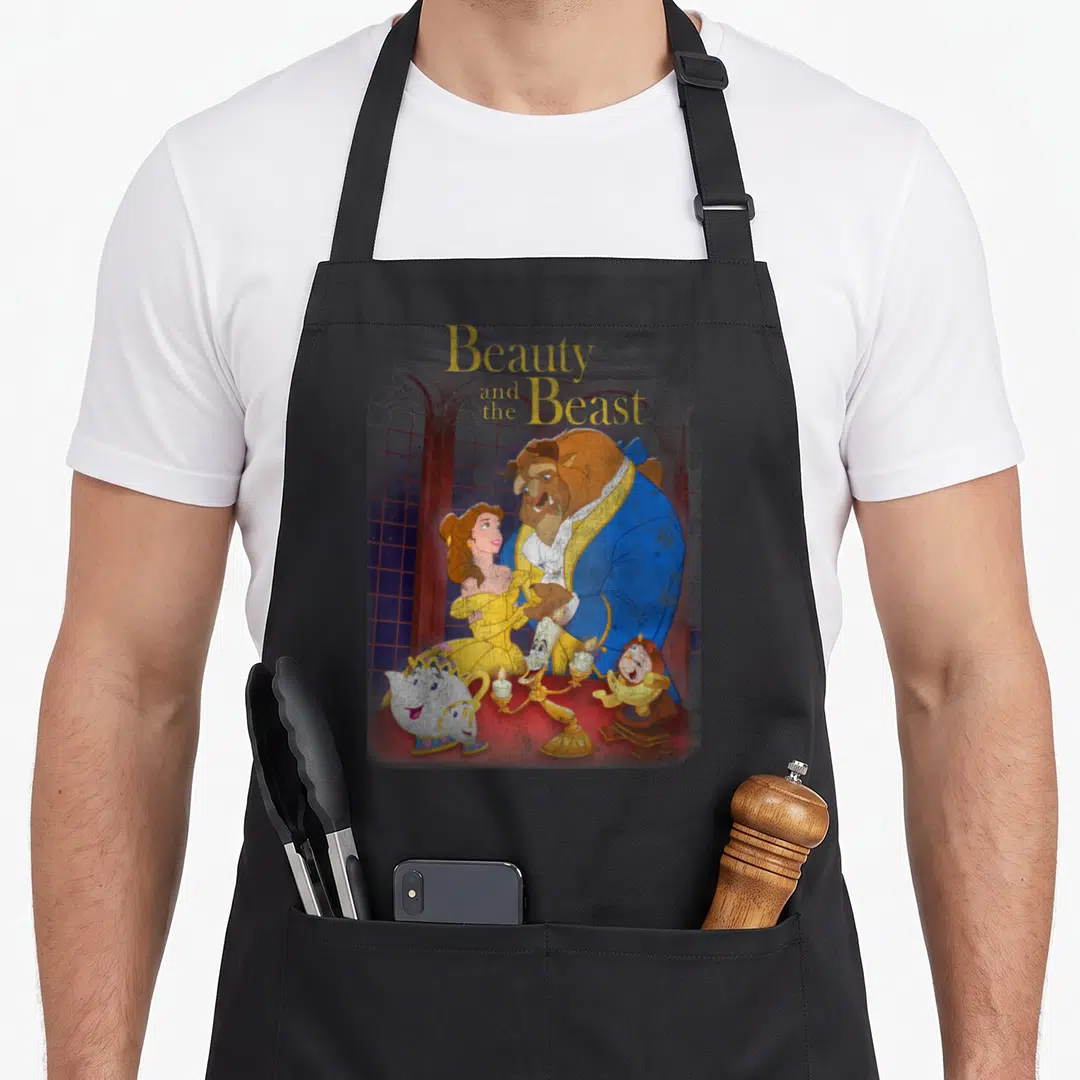Shot distressed apron - Beauty and the Beast title above Beast Belle and talking objects on red table with arched — shown on a black cotton canvas apron against a white background
