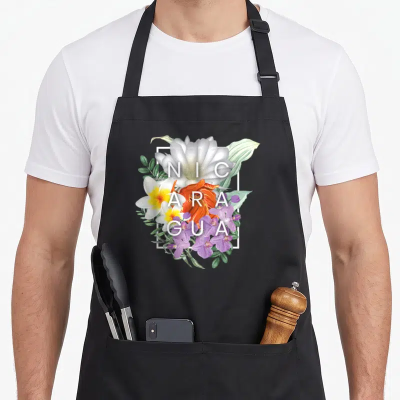 Nicaragua pride apron - Vertical floral cluster with NIC ARA GUA text in white square frame — shown on a black cotton canvas apron against a white background
