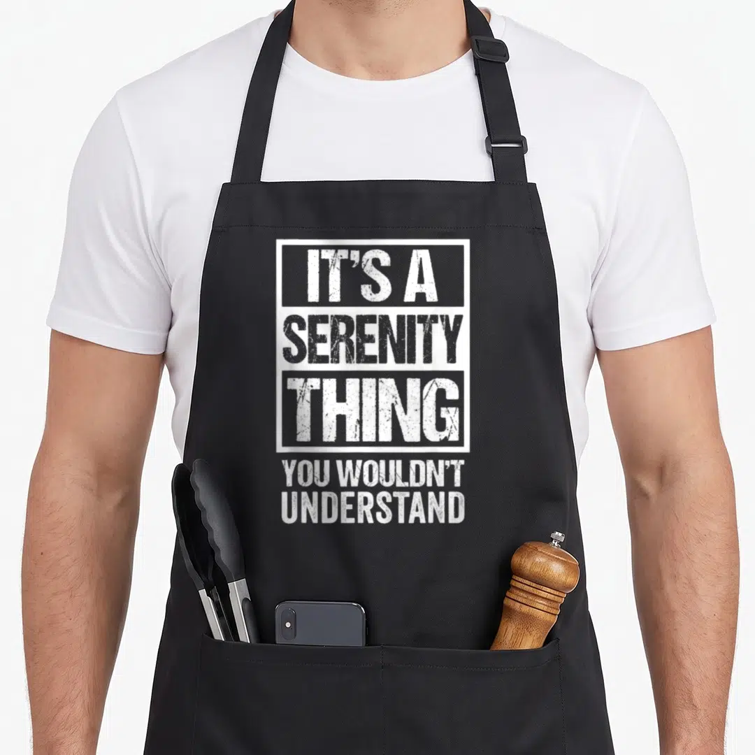 Vintage serenity apron - White text IT'S A SERENITY THING YOU WOULDN'T UNDERSTAND stacked vertically with a box around — shown on a black cotton canvas apron against a white background