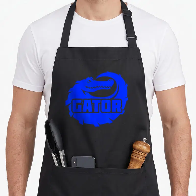 Funny gatorade apron - Blue alligator curled in circle with GATOR text across body — shown on a black cotton canvas apron against a white background
